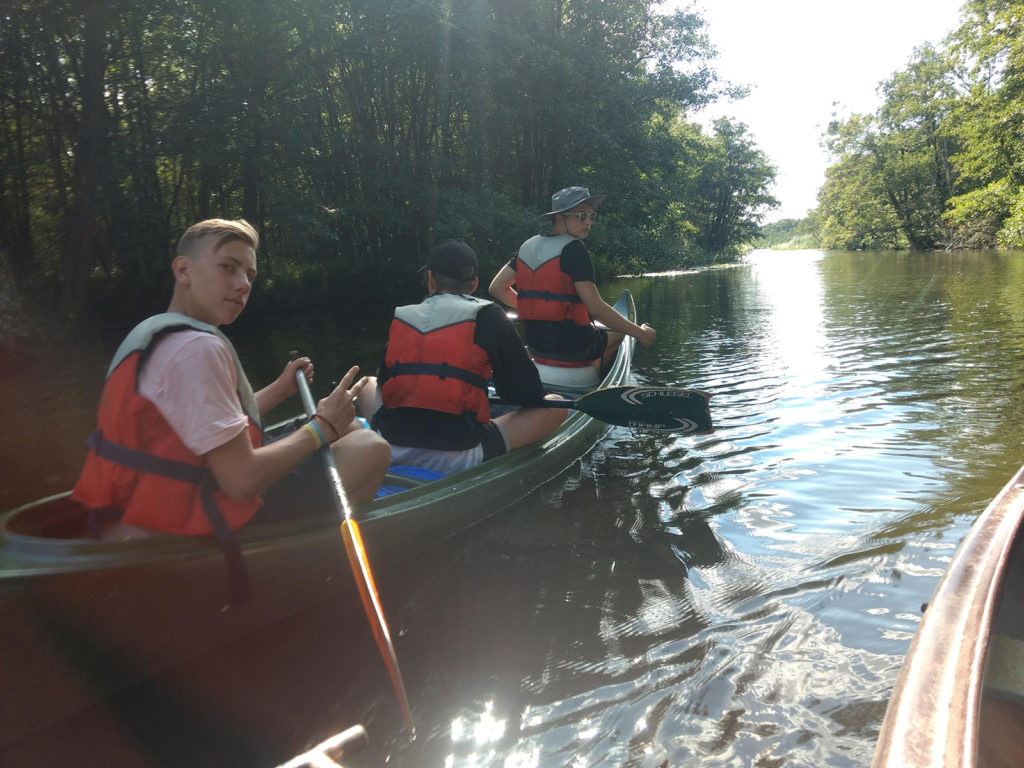 Jugendliche mit Schwimmwesten sitzen in einem Kanu auf einem Fluß.